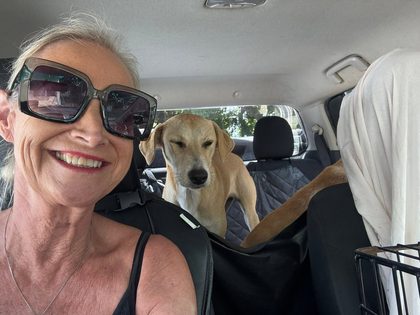 Woman taking a selfie in a car with a tan dog standing in the back seat