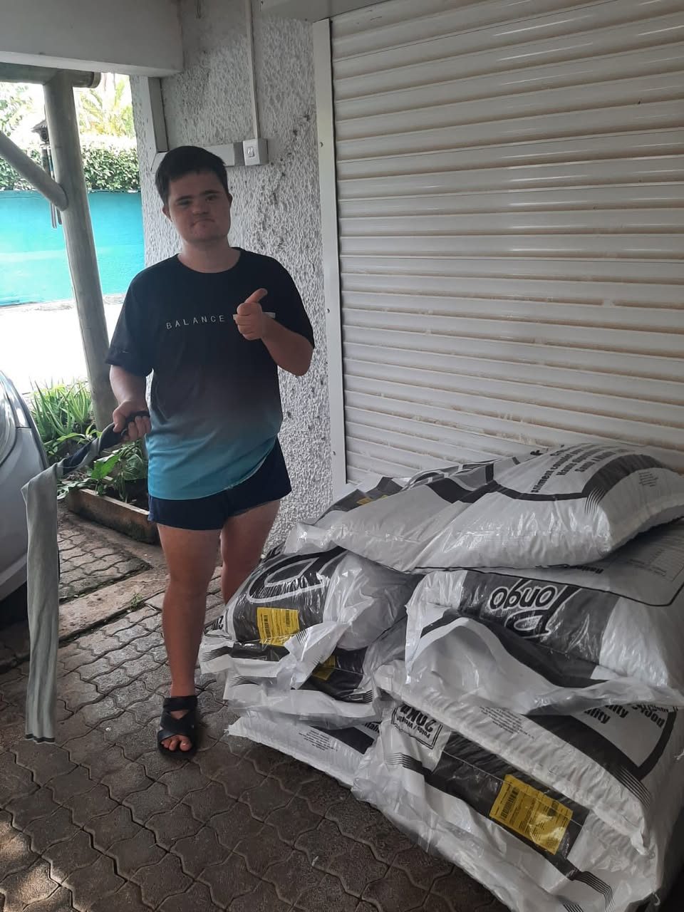 Man giving a thumbs up beside stacked bags of animal feed outside a shuttered storefront