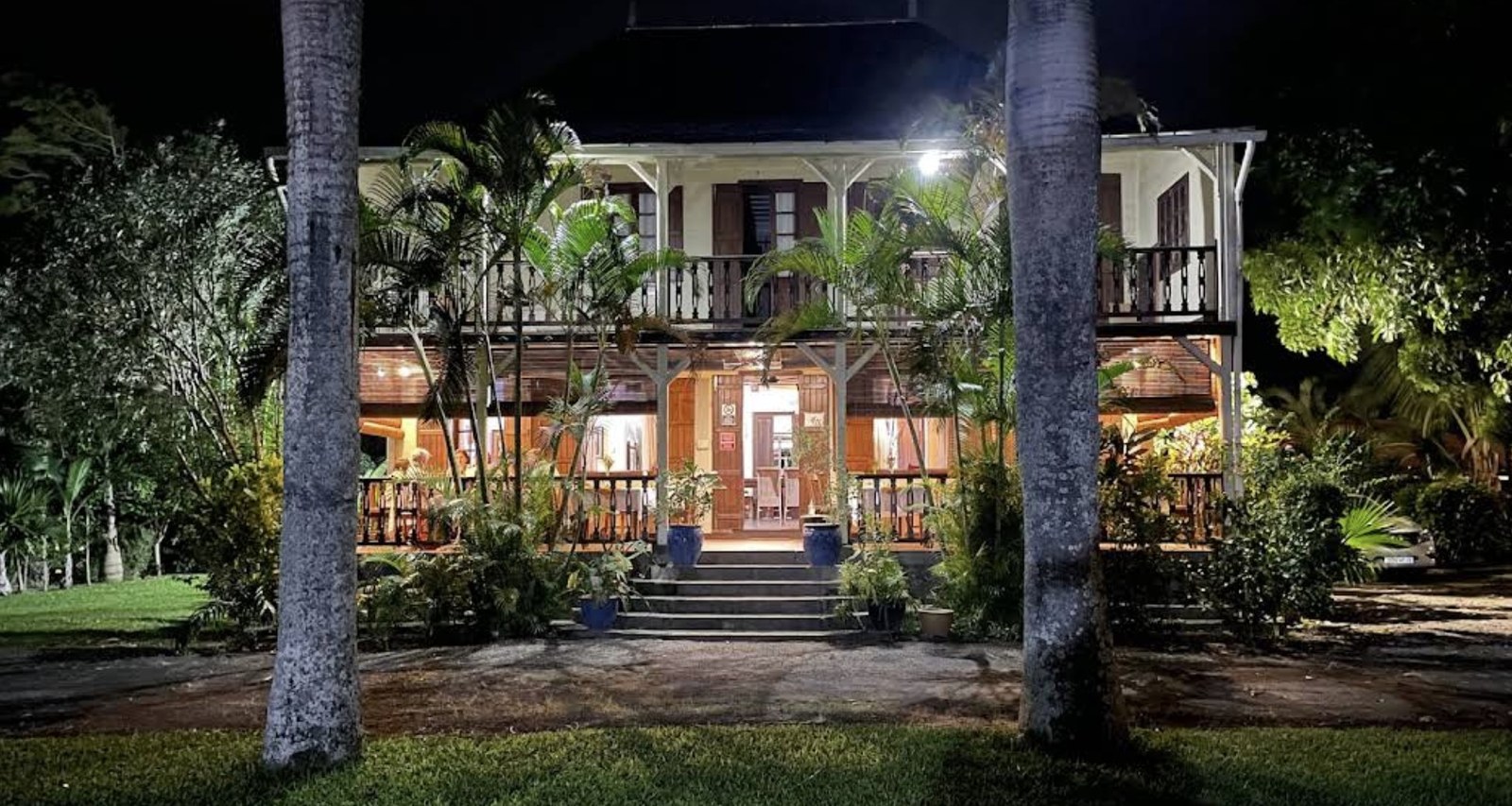 Le Jardin de Beau Vallon lit up at night, its veranda open between the palms